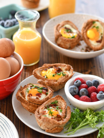 A breakfast table set with a plate of Egg and Toast Cups, surrounded by OJ, blueberries and a bowl of eggs.