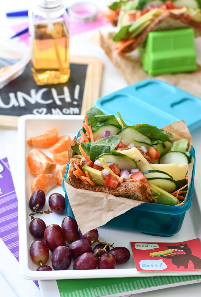 4 hummus and veggie sandwich tacos being held by taco holders with a lunchbox theme