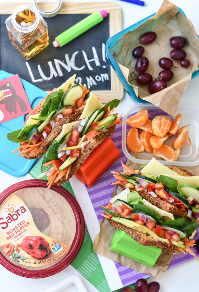 4 hummus and veggie sandwich tacos being held by taco holders with a lunchbox theme with sabra hummus.